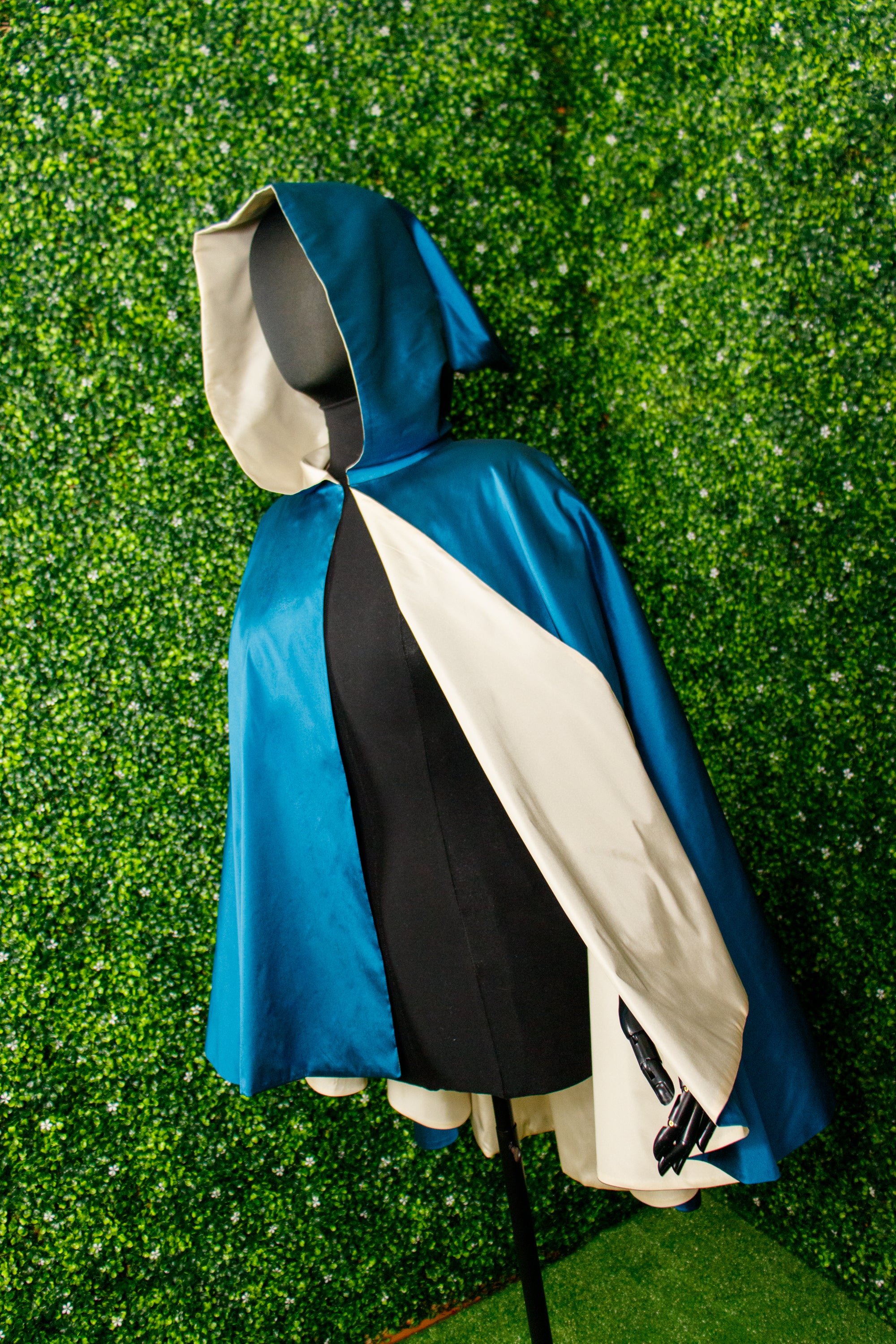 Blue cape with a cream lining on a mannequin in front of a green background