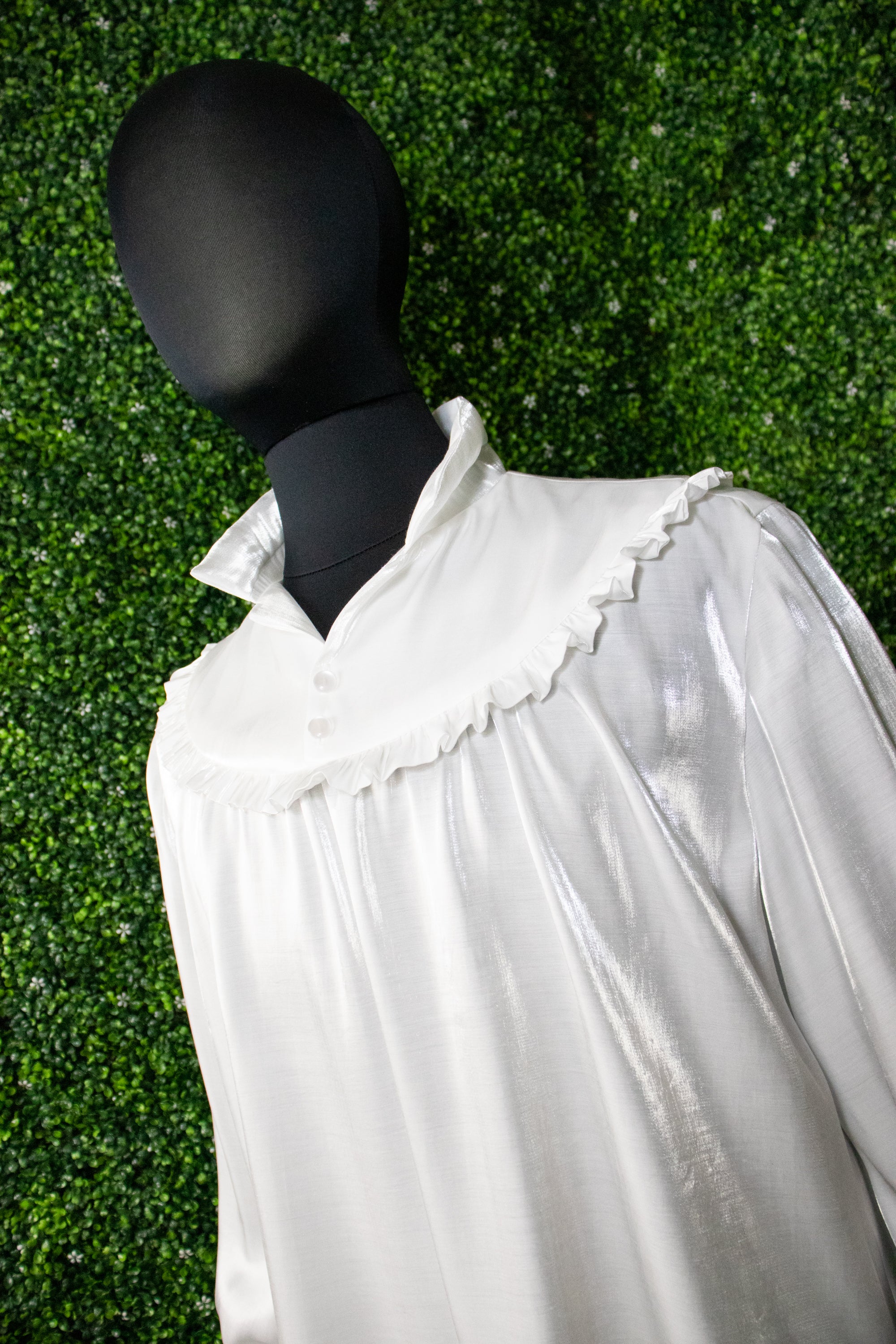 White shirt with ruffle on a mannequin in front of a green background