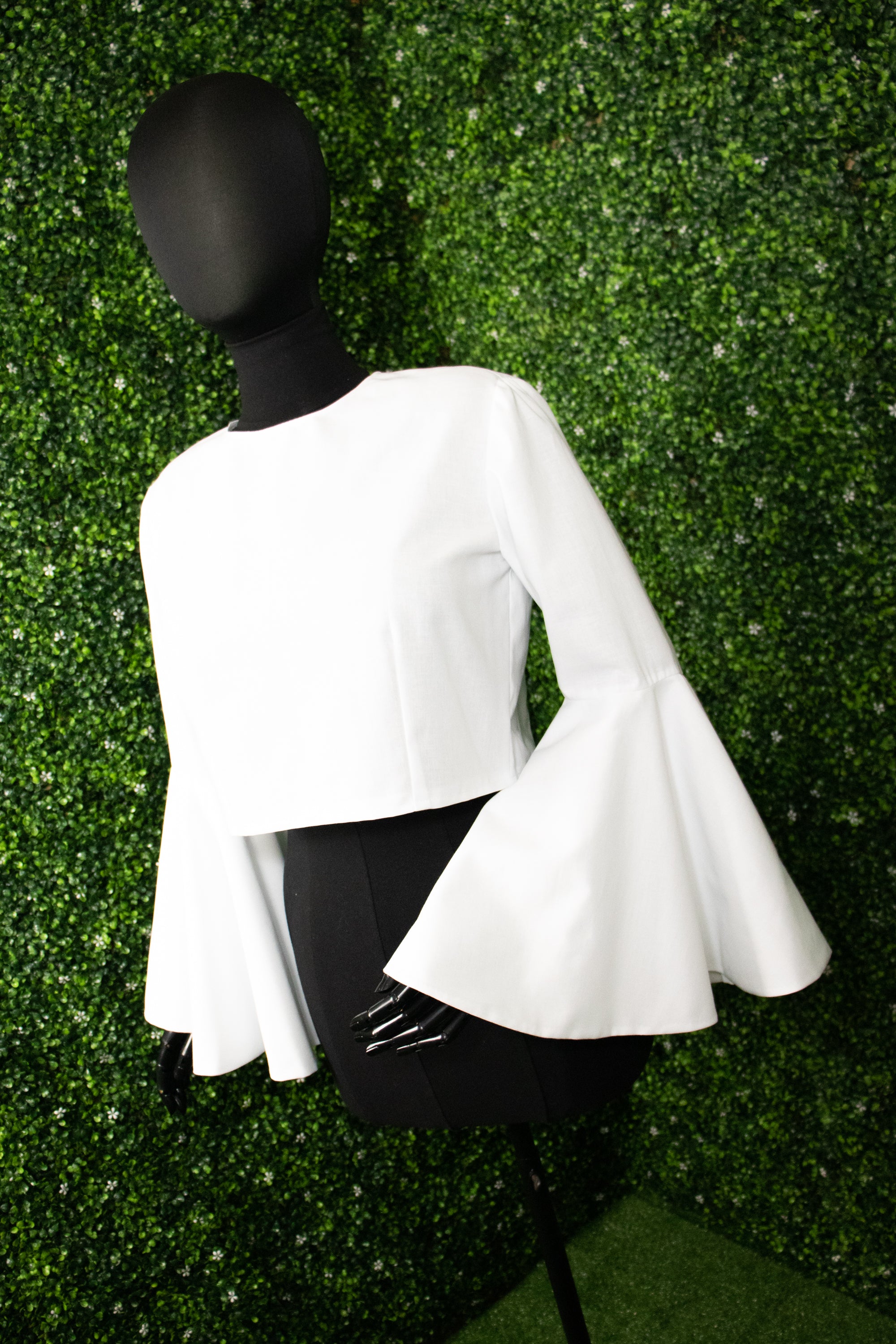 White shirt with bell sleeves on a mannequin in front of a green background