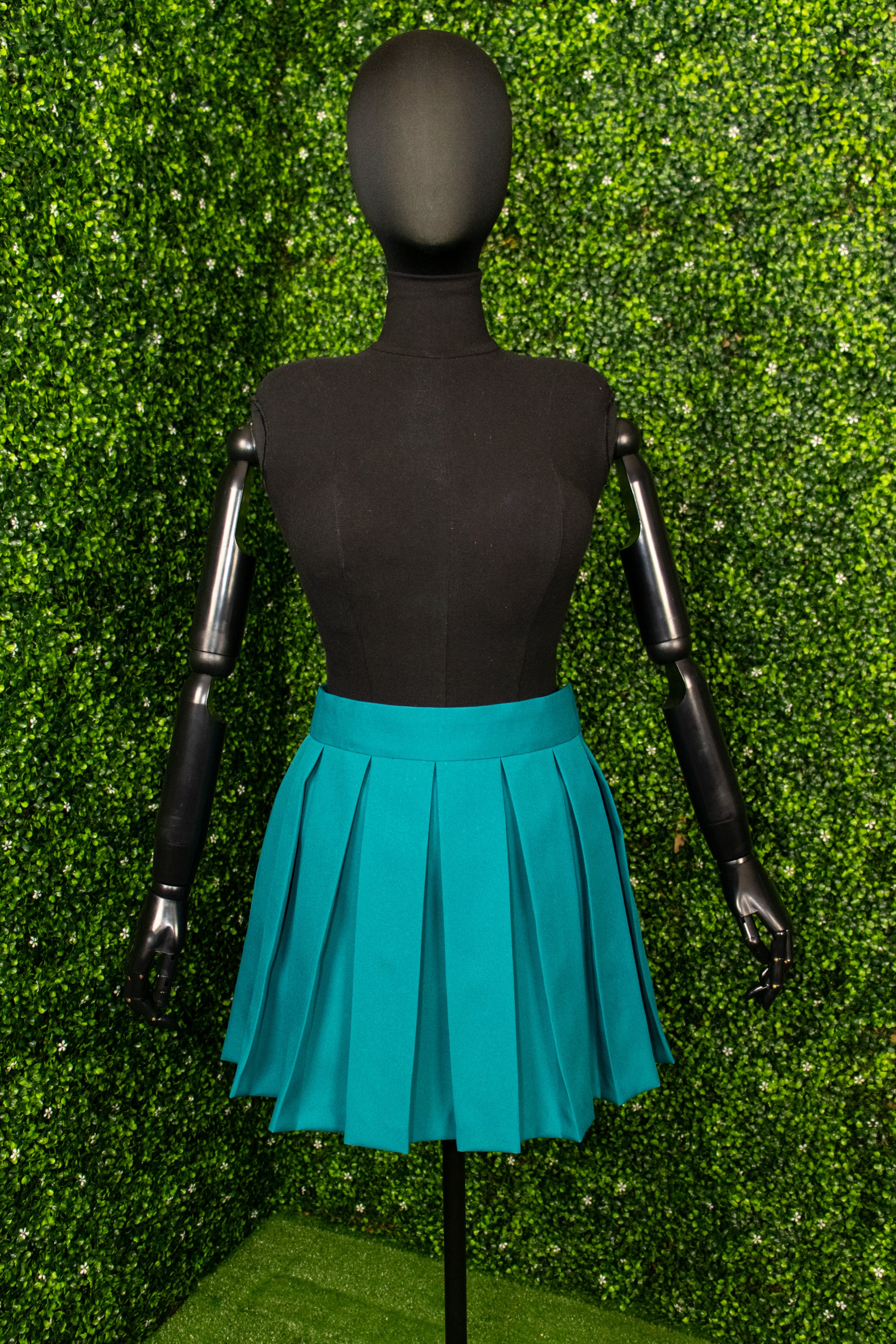 Short teal pleated skirt on a mannequin in front of a green background